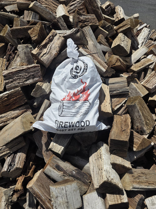 Mixed Hardwood Firewood 20kg Bag placed on a stack of chopped firewood logs.