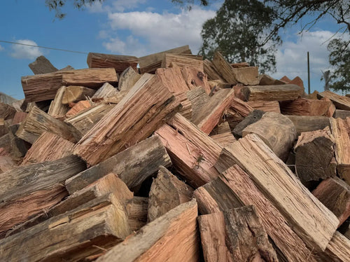 Mixed Hardwood Firewood 1m³ Bag stacked in a pile, showcasing various pieces of wood under a blue sky.